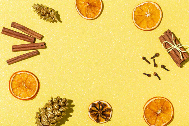 Новогодняя и рождественская композиция на блестящем желтом фоне. Flat lay, top view arrangement of dried orange rings, cinnamon, гвоздика, golden pine cones. Ингредиенты для глинтвейна. - Фото, изображение