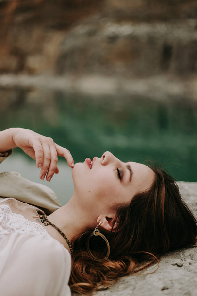 Nehrin yanındaki kayalıklarda beyaz elbiseli güzel bir kız yatıyor.  - Fotoğraf, Görsel
