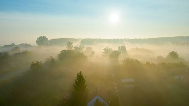 Αεροφωτογραφία πάνω από οικισμό εξοχικό σπίτι, δάσος, βλάστηση τοπίου κατά την ανατολή του ηλίου στην ομίχλη του φθινοπώρου. - Φωτογραφία, εικόνα