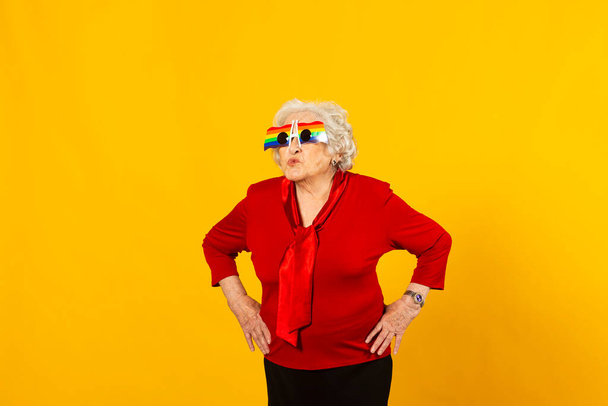 Студійний портрет старшої жінки в червоній сорочці та сонцезахисних окулярах веселки на жовтому тлі
 - Фото, зображення