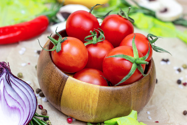 Fresh red ripe cherry tomatoes in wooden bowl with salad leaves, onion, pepper, champignon mushrooms, spices and salt on light food background. - Foto, imagen