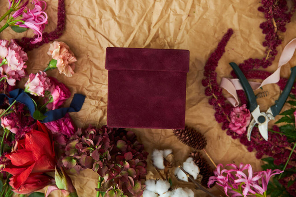 The red gift box with a place for text is framed by flowers and things of the florist on craft parchment paper - Photo, Image