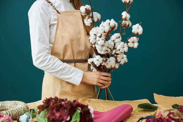 A woman florist in working clothes creates a bouquet - 写真・画像