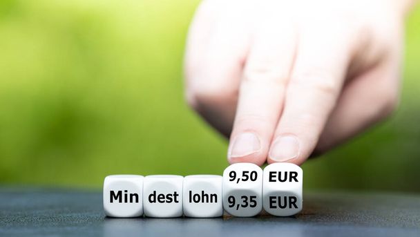 Hand turns dice and changes the German expression "Mindestlohn 9.30 EUR" to "Mindestlohn 9.50 EUR" (minimum wage 9.50 EUR). - 写真・画像