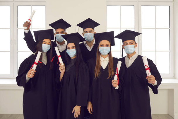 Груповий портрет випускників змішаної раси в масках для обличчя, які тримають свої дипломи
 - Фото, зображення