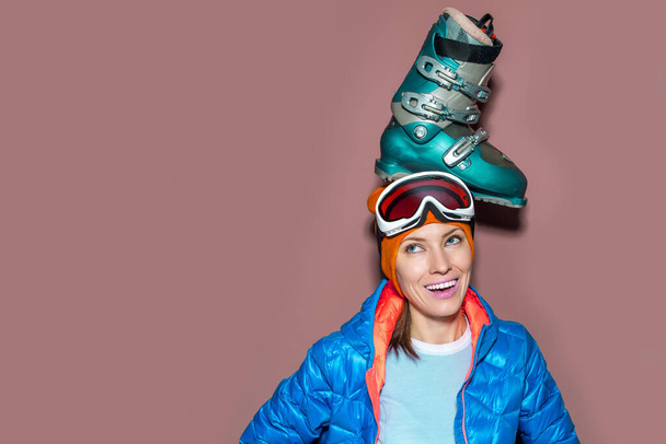 Sporty girl wearing winter clothes , goggles, holding ski sticks and a ski boot at home - Foto, immagini