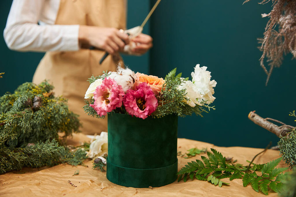 A female florist creates a bouquet for Christmas from flowers and branches of spruce. The work of a florist. - 写真・画像