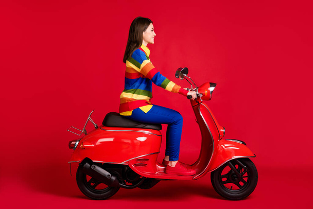 Προφίλ πλευρά άποψη της ελκυστικής χαρούμενο κορίτσι οδήγηση ποδήλατο πρόκειται για περιοδεία ελεύθερο χρόνο απομονώνονται σε φωτεινό κόκκινο χρώμα φόντο - Φωτογραφία, εικόνα