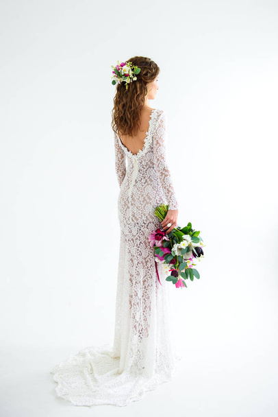 joyful girl bride in a white knitted dress posing with a bouquet of flowers in the studio on a white background - Photo, Image