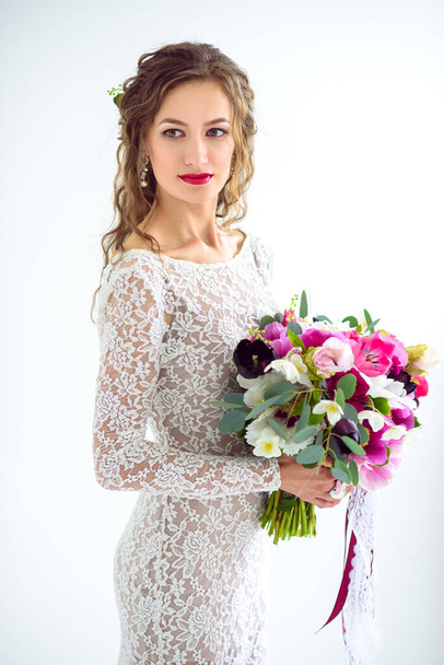 joyful girl bride in a white knitted dress posing with a bouquet of flowers in the studio on a white background - Fotografie, Obrázek