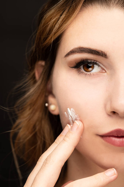 Estudio de una joven mujer aplicando crema facial - Foto, imagen