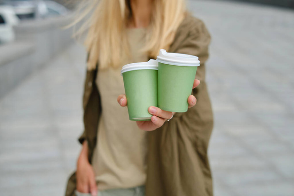 Green paper cup with coffee in woman hand. Time for drink coffee in city. Coffee to go. Enjoy moment, take a break. Disposable paper cup closeup. Delicious hot beverage. Blank space for text, mockup - Valokuva, kuva