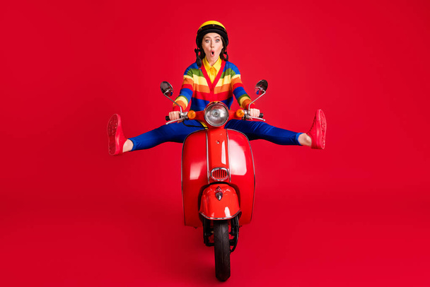 Photo portrait of shocked girl spreading legs like star riding retro scooter isolated on vivid red colored background - Zdjęcie, obraz