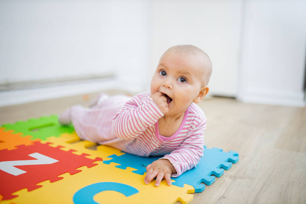 Adorabile bambino sdraiato su un tappeto colorato con il pugno in bocca - Foto, immagini