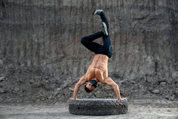 Shirtless bodybuilder training handstand on large wheel - Photo, image