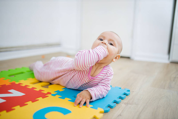 Чарівна дитина лежить на барвистому килимку з кулаком в роті
 - Фото, зображення