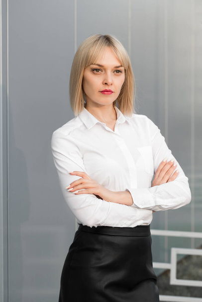 Successful beautiful cheerful young businesswoman or student girl with crossed arms in white shirt and black skirt standing against grey background - Zdjęcie, obraz
