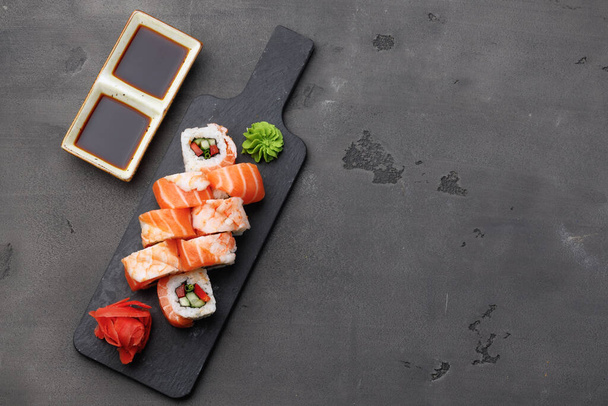Vista superior del rollo de sushi con salmón y gambas sobre fondo negro - Foto, Imagen