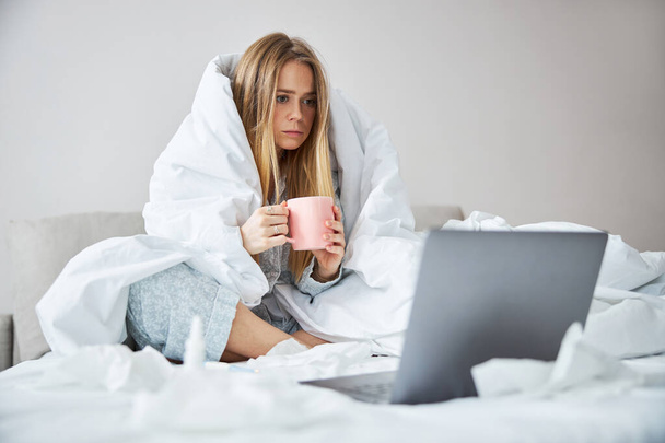 Young woman with flu drinking tea and using notebook at home - Foto, immagini