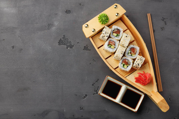 Sushi roll served on wooden boat plate on black background - Foto, imagen