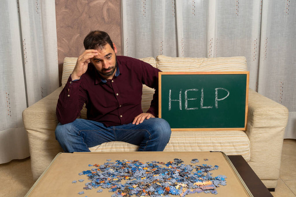 Młody człowiek z brodą siedzący na kanapie w domu i układający puzzle. Koncepcja rozrywki - Zdjęcie, obraz