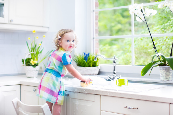 κορίτσι πλύσιμο των πιάτων, καθαρισμός με ένα σφουγγάρι και να παίζει με αφρό - Φωτογραφία, εικόνα