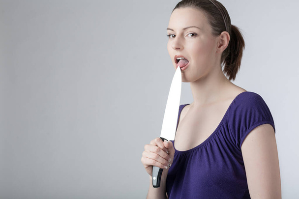 A young woman is licking at a sharp kitchen knife  - Photo, Image