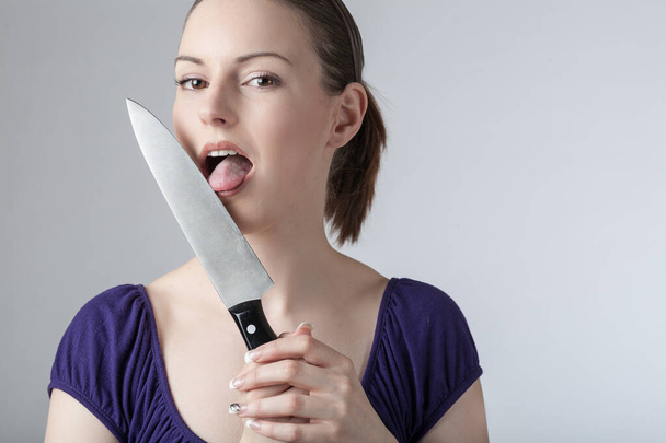 Une jeune femme lèche un couteau de cuisine pointu  - Photo, image