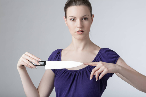 Μια νεαρή γυναίκα παίζει με ένα κοφτερό μαχαίρι κουζίνας.  - Φωτογραφία, εικόνα