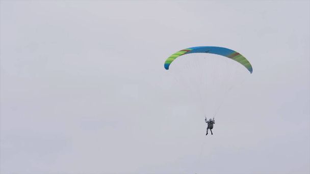 Нижний вид человека с парашютом в небе. Начали. Человек летает в небе на параплане в облачную погоду. Экстремальные виды спорта и парашюты - Фото, изображение