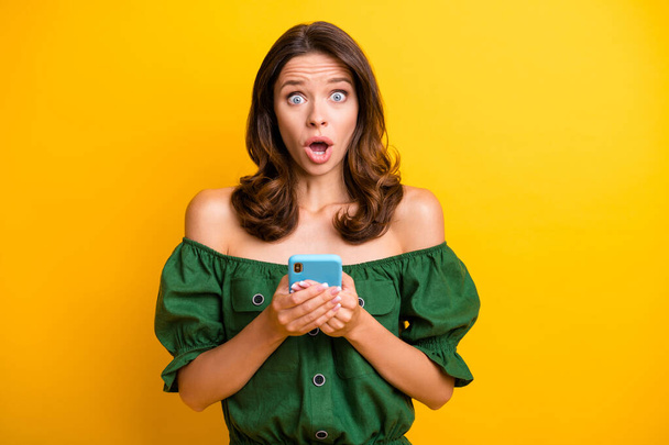 Photo of astonished young woman wear off-shoulder blouse hold phone reaction news isolated on yellow color background - Фото, изображение