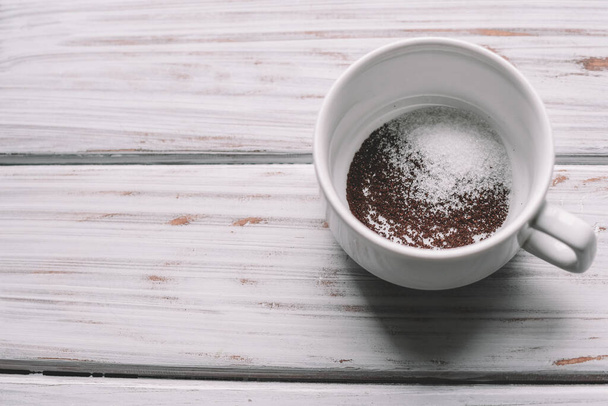 Kawa mielona z cukrem w białym kubku na jasnym drewnianym tle. Widok z góry.Międzynarodowy dzień kawy. - Zdjęcie, obraz