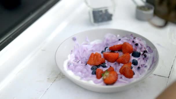 Mano femenina añadiendo fresas a un tazón de yogur - Metraje, vídeo