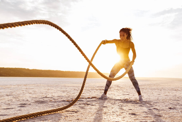 Image of strong african american sportswoman working out with battle ropes on nature - Фото, изображение
