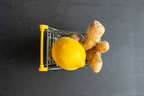 limón y jengibre en un carrito de la compra sobre un fondo gris oscuro vista superior - Foto, imagen
