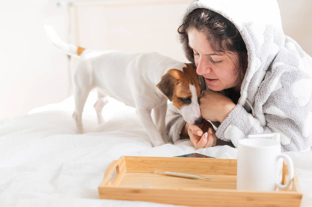 Woman in pajamas lies in bed with a small dog jack russell terrier. Love betweeen pet and owner - Foto, Bild