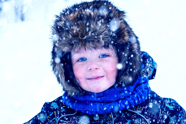 Piękna, uśmiechnięta twarz małego chłopca w zimowych klapkach na kapelusze. Duże oko. Patrząc w kamerę z bliska. - Zdjęcie, obraz