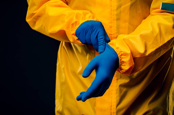 The scientist wears a yellow decontamination suit and wears blue rubber gloves to protect his skin - Photo, Image