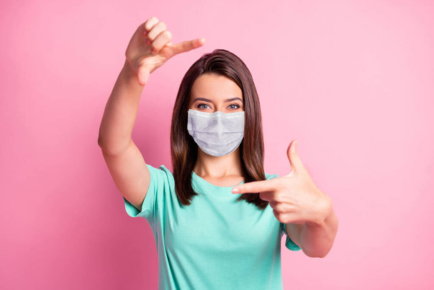 Photo portrait of pretty girl showing frame made of fingers in teal fabric face mask isolated on pastel pink colored background - Foto, Imagem