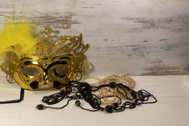 Sobre un fondo claro se encuentra una máscara de carnaval con una pluma amarilla y cuentas negras y claras. - Foto, Imagen