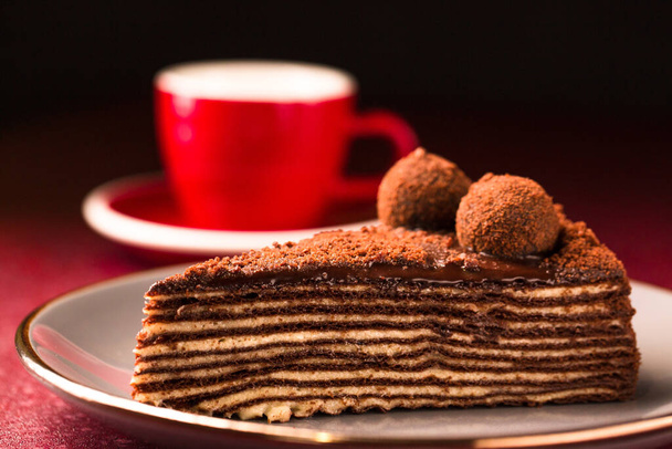 Pastel de chocolate multicapa Spartak con una taza de café sobre un fondo oscuro - Foto, Imagen