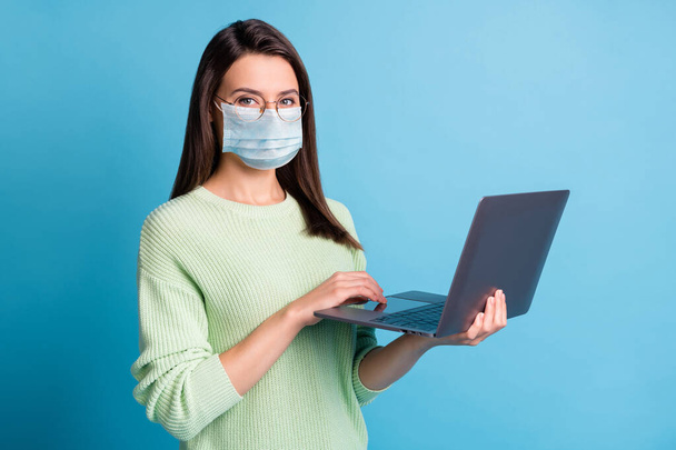 Photo of positive girl working on laptop wear blue face mask isolated over blue color background - Valokuva, kuva