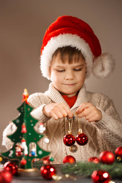 Boy in santa hat decorates wooden vintage christmas tree with toys - Photo, Image