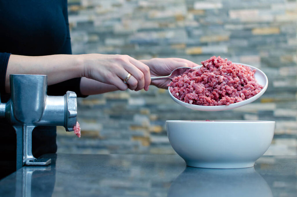 Une femme fait du bœuf haché ou du porc sur un vieux hachoir manuel en métal. Morceaux de viande rouge fraîche pour la viande hachée dans un bol blanc. - Photo, image