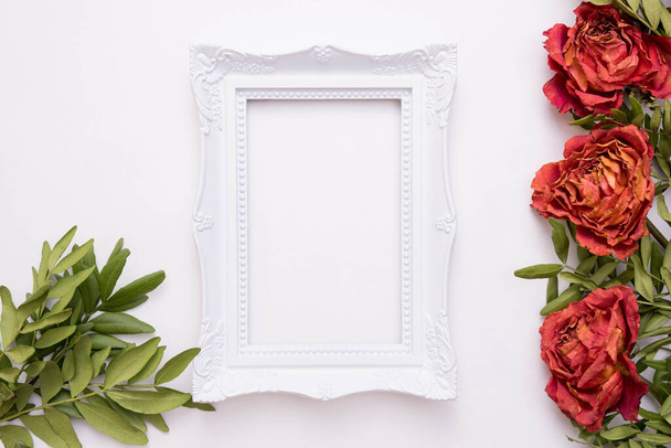 live and dead roses lie on a white background, in the middle there is a photo frame, top view - Photo, Image