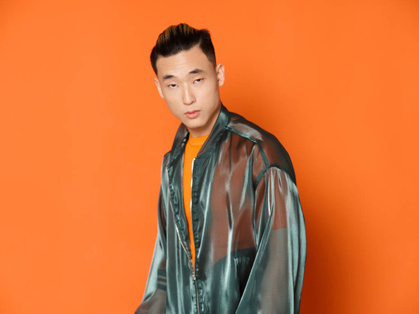 Asian man wearing orange t-shirt over isolated background and gray jacket model - Zdjęcie, obraz
