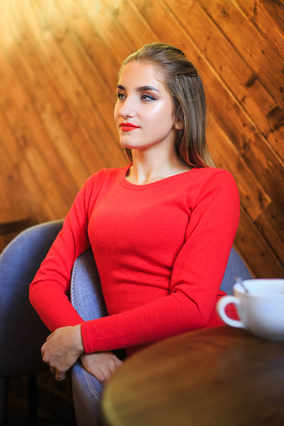 Egy vörös ruhás fiatal nő portréja, aki egy széken ül egy kávézóban. - Fotó, kép
