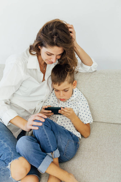 Mama i syn grają w smartfona na kanapie - Zdjęcie, obraz