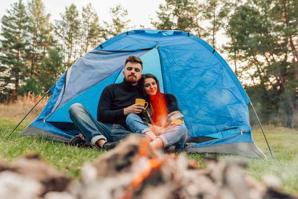 couple heureux assis à l'entrée de la tente avec des tasses dans leurs mains. voyageurs boivent du thé à l'extérieur - Photo, image