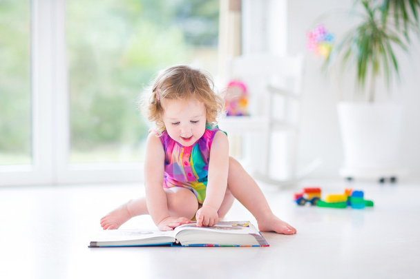 Toddler girl reading a book sitting on a fllor - Photo, Image